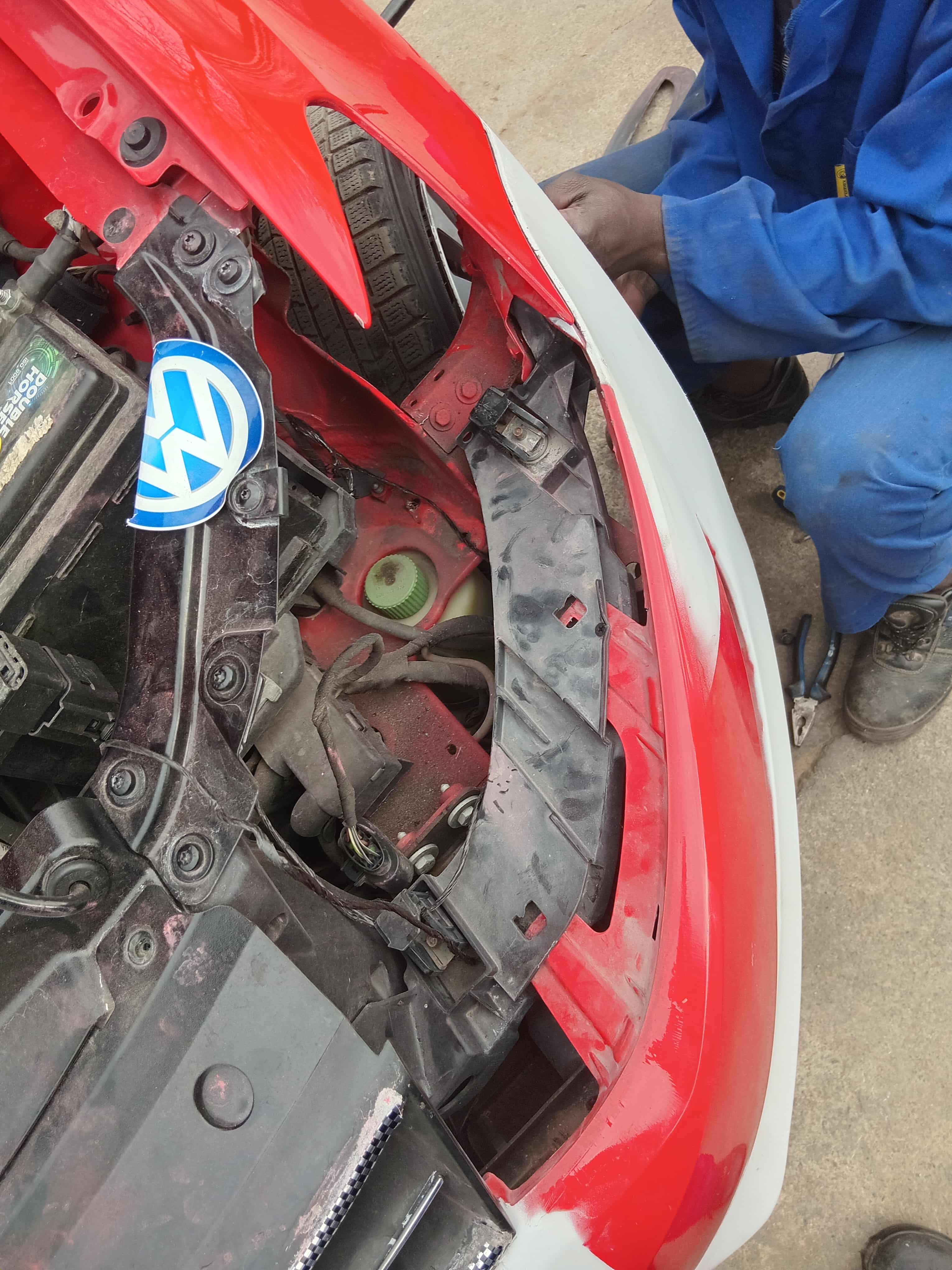 Technician working beside a partially prepared red vehicle bumper